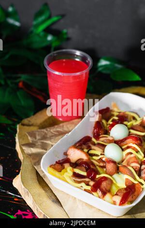 cuisine de rue colombienne, salchipapa servi sur un plateau en bois avec un verre de jus de fruits rouges à côté. restauration rapide avec pommes de terre, saucisses, œufs et sauces. Banque D'Images