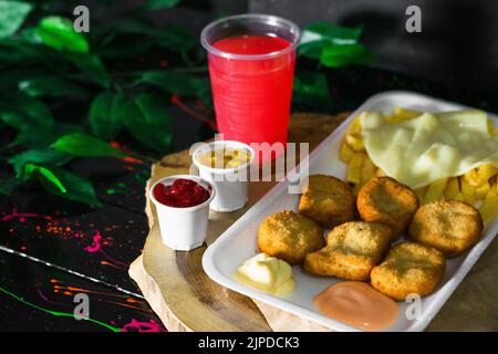 Cuisine de rue colombienne, assiette de nuggets de poulet avec pommes de terre et fromage mozzarella, servi sur un plateau en bois avec un verre de jus de fruits rouges sur le si Banque D'Images