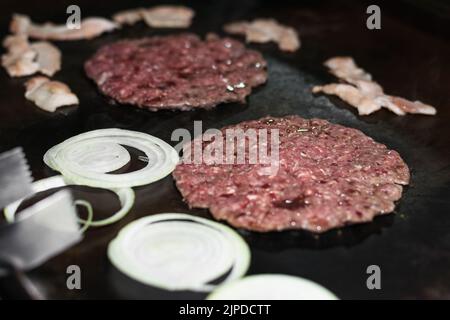 gros plan de deux viandes hachées de hamburger avec oignon et tosino autour, cuisant dans un grill colombien de rue ou un fast-food stand, bœuf sur Banque D'Images