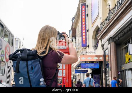 LONDRES - 18 mai 2022: Une femme photographiant Retour à l'avenir, les signes musicaux et la boîte téléphonique britannique traditionnelle à l'extérieur du théâtre Adelphi sur le Banque D'Images