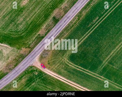 La voiture rouge se garer sur le terrain vert près de la route asphaltée. Vue aérienne de dessus en bas, thème de l'agriculture. Couleur verte fraîche au printemps pendant le coucher du soleil. R Banque D'Images