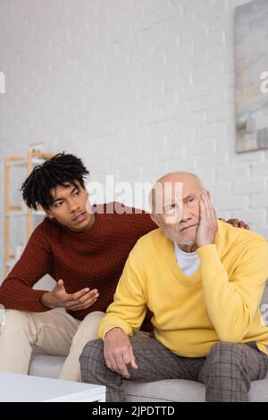 Un homme âgé contrarié assis près du petit-fils afro-américain qui parle à la maison Banque D'Images