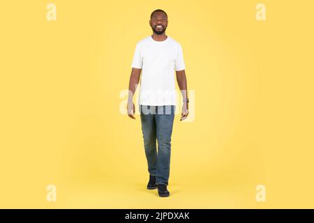Pleine longueur de Happy Black Male marchant sur fond jaune Banque D'Images