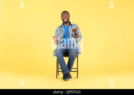 Africain américain Homme parlant assis dans la chaise sur fond jaune Banque D'Images