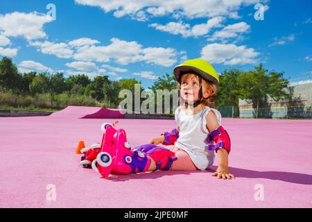 Petite fille apprendre à skate rouleaux, s'asseoir souriant sur le sol Banque D'Images