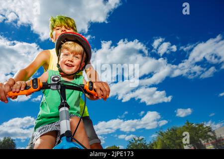 Gros plan image grand garçon pousser petit frère enseigner à faire un vélo Banque D'Images