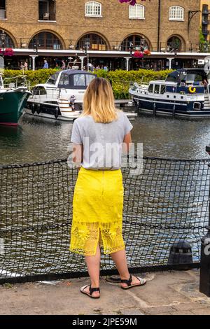 une jeune femme se tenant au quai st katherine dans le centre de londres, regardant sur l'eau et les bateaux, une jeune femme portant une robe jaune vif rêvant de jour. Banque D'Images