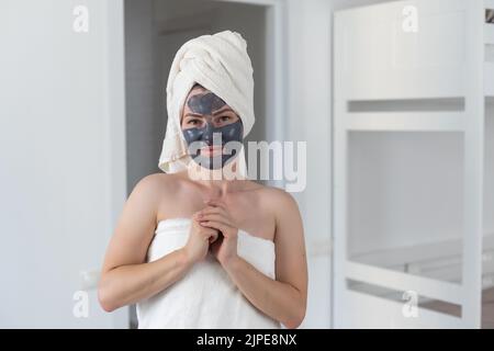 Femme enlevant masque de boue d'argile sèche faciale avec éponge dans la salle de bains devant le miroir. Soins de la peau. Fille prenant soin de son teint. Spa de beauté Banque D'Images