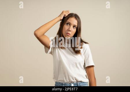 Portrait d'une fille brune ou d'une jeune femme avec une expression perplexe, perplexe, stupide et ignorante sur le visage en grattant la tête avec la main. Quand vous ne savez pas Banque D'Images