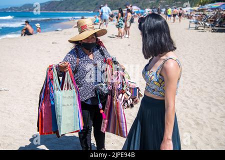 A vendor selling souvenirs to a woman on a beach in Sayulita, Mexico Stock Photo