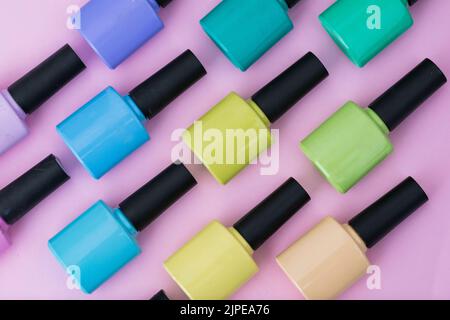 Vue de dessus d'un motif de vernis à ongles de différentes couleurs placé sur un fond rose, violet, bleu, vert et jaune. Éléments pour faire un tableau an Banque D'Images