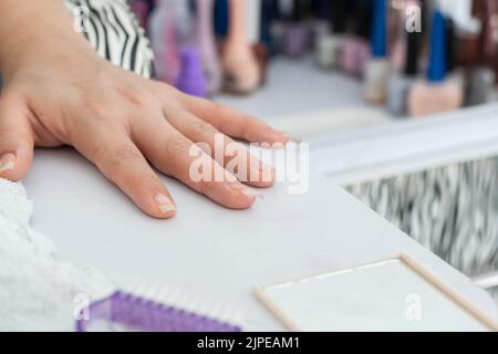 détail de la main de la fille latine, placé sur la table de manucure, prêt à commencer à peindre et à décorer les ongles. en arrière-plan beaucoup de vernis colorés. Banque D'Images