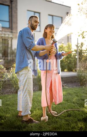 Beau couple arroser la pelouse à l'arrière-cour Banque D'Images