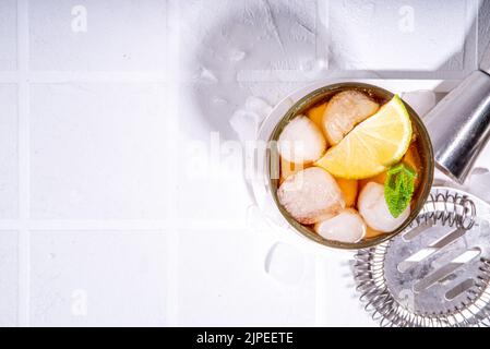 Cocktail au rhum, au citron vert et au cola Cuba libre. Boisson froide de Coca-Cola d'été avec jus d'agrumes, glaçons et feuilles de menthe, carrelage blanc soleil fond éclairé c Banque D'Images