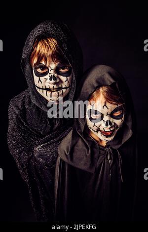 Deux enfants portent des robes sombres et de la peinture effrayante pour le visage à Halloween. Banque D'Images