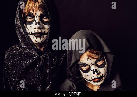 Deux enfants portent des robes sombres et de la peinture effrayante pour le visage à Halloween. Banque D'Images