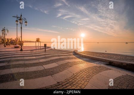 Une photo au coucher du soleil du remblai du lac de Garde en Italie de Lazise avec un sol rayé et un soleil rayés qui brillent à l'horizon Banque D'Images