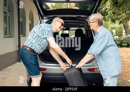 Les personnes âgées mettent des sacs dans le coffre du véhicule pour partir en vacances-retraite pendant l'été. Voyage sur route pour les loisirs, bagages d'emballage et valise pour les vacances urbaines en ville. Banque D'Images