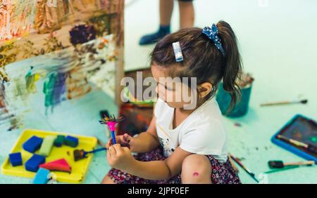 Peinture de film adhésif. Petite fille tout-petit peindre avec une éponge, des pinceaux et des peintures sur un film adhésif enroulé tout autour de l'étagère en bois. Activité créative pour le développement des enfants à l'école maternelle. Photo de haute qualité Banque D'Images