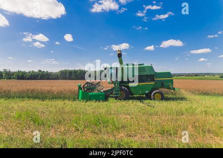 Vue latérale d'un drone aérien d'une moissonneuse-batteuse agricole verte avec un rabatteur rotatif récolte dans un grand champ dans une zone rurale par une chaude journée ensoleillée. Photo de haute qualité Banque D'Images