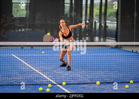 Femme jouant de padel dans un terrain de padel d'herbe bleue intérieur - jeune femme sportive joueur de padel frappant le ballon avec une raquette Banque D'Images