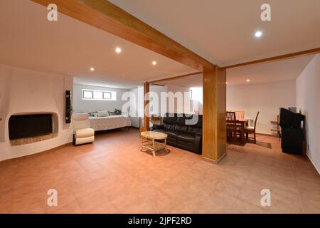 Séjour d'une maison familiale simple avec carrelage, canapés en cuir noir et cheminée intégrée, table à manger en bois avec chaises et buffets Banque D'Images