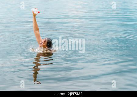 Sortir de l'eau personne succès homme gagnant moment. Sauver la pollution plastique de l'océan. Bras soulevé main tenant bouteille plastique poubelle pollution de plage Banque D'Images