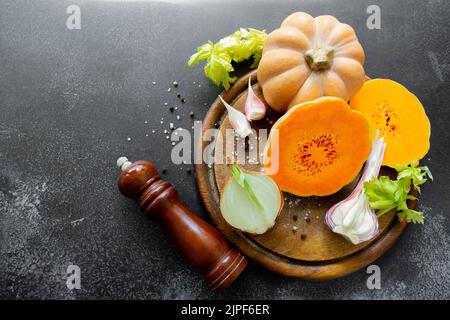 Les légumes frais et lumineux sont disposés sur une planche à découper en bois : courge de noyer cendré, feuilles de céleri vertes. Arrière-plan noir inégal, espace de copie. Banque D'Images