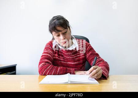 Femme d'affaires latine assise à son bureau pour prendre des notes Banque D'Images