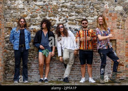 Les membres d'un groupe Rock posent devant un vieux mur de briques. Un homme tient une feuille de figuier par son aine tandis que d'autres tirent les visages Banque D'Images