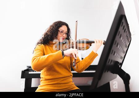 Brunette femme portant un chandail jaune, et jouant du violon en lisant de la musique en feuilles. Banque D'Images
