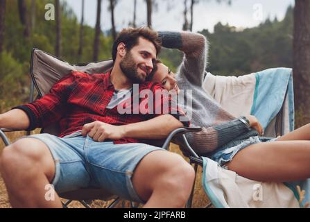 Jeune couple aimant assis sur une chaise dans leur camping. Un jeune homme et une femme heureux campant dans la nature. Banque D'Images