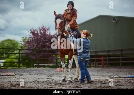 Rien ne dit rêve d'enfance comme apprendre à monter un poney. Un entraîneur enseignant à une adolescente comment monter un cheval sur une ferme. Banque D'Images