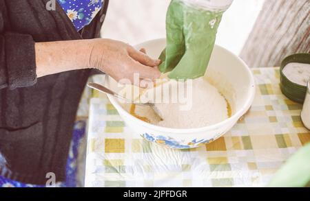 Grand-mère verser la farine dans la pâte à crêpes Banque D'Images