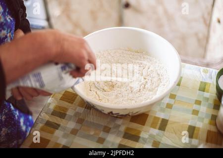 Grand-mère versant du lait dans de la pâte à crêpes Banque D'Images