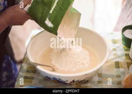 Grand-mère verser la farine dans la pâte à crêpes Banque D'Images