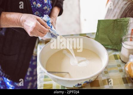 Grand-mère versant du lait dans de la pâte à crêpes Banque D'Images