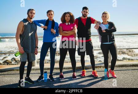 Une équipe moyenne. Portrait d'un jeune groupe joyeux d'amis debout ensemble avant un exercice de forme physique dehors pendant la journée. Banque D'Images