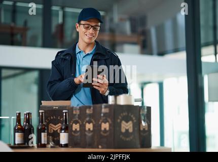 Le stock prend sur mon appareil. Un beau jeune homme prend l'inventaire des articles qu'il doit livrer aux clients. Banque D'Images