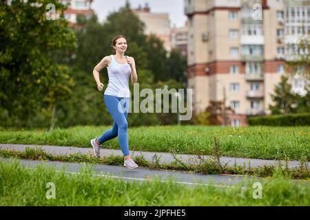 jogging féminin de 30 ans dans une zone garée de zone résidentielle avec immeubles d'appartements. Banque D'Images