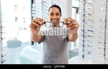 Femme tenant une paire de lunettes tendance, de lunettes élégantes et de verres correcteurs chez un optométriste. Portrait d'un client qui choisit, achète et Banque D'Images