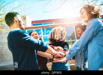 Ils connaissent mieux l'ensemble. Un groupe diversifié d'amis d'université debout dehors avec leurs mains dans un caucus. Banque D'Images