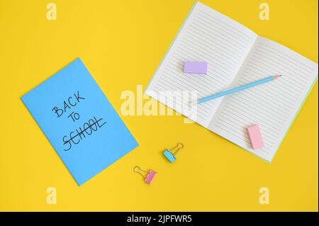 vue de dessus du texte de retour à l'école écrit dans la couverture d'un bloc-notes bleu, bloc-notes ouvert, crayon, gomme, clip dans des couleurs pastel Banque D'Images