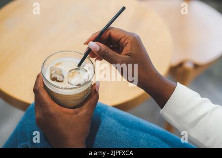 Belles mains de femme afro-américaine avec latte froide dans le café. Pause café. Latte à café avec glace. Ambiance café en été. Banque D'Images