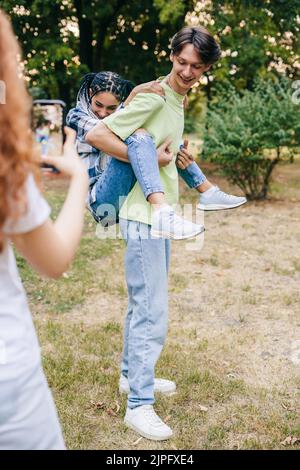 La jeune femme filmant une vidéo sur le tik tok avec un ami, comment il porte son collègue derrière. J'ai apprécié de prendre des selfies avec un smartphone. Vidéo verticale Banque D'Images