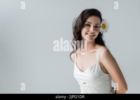 Bonne femme brune avec camomille dans les cheveux regardant la caméra isolée sur gris Banque D'Images