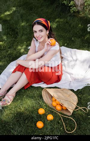 Vue en grand angle d'une femme gaie tenant une couverture orange dans le parc Banque D'Images