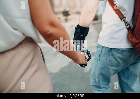 Jeune homme handicapé avec une main artificielle prothétique marchant et tenant la main de petite amie de femme Banque D'Images