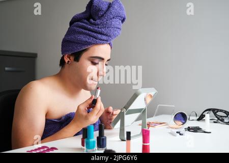Jeune homme transgenre appliquant le rouge à lèvres. Banque D'Images