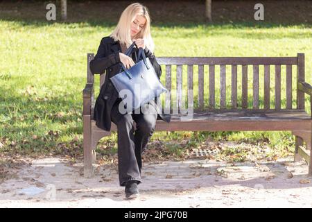 femme blonde assise sur un banc de parc vêtue de noir Banque D'Images